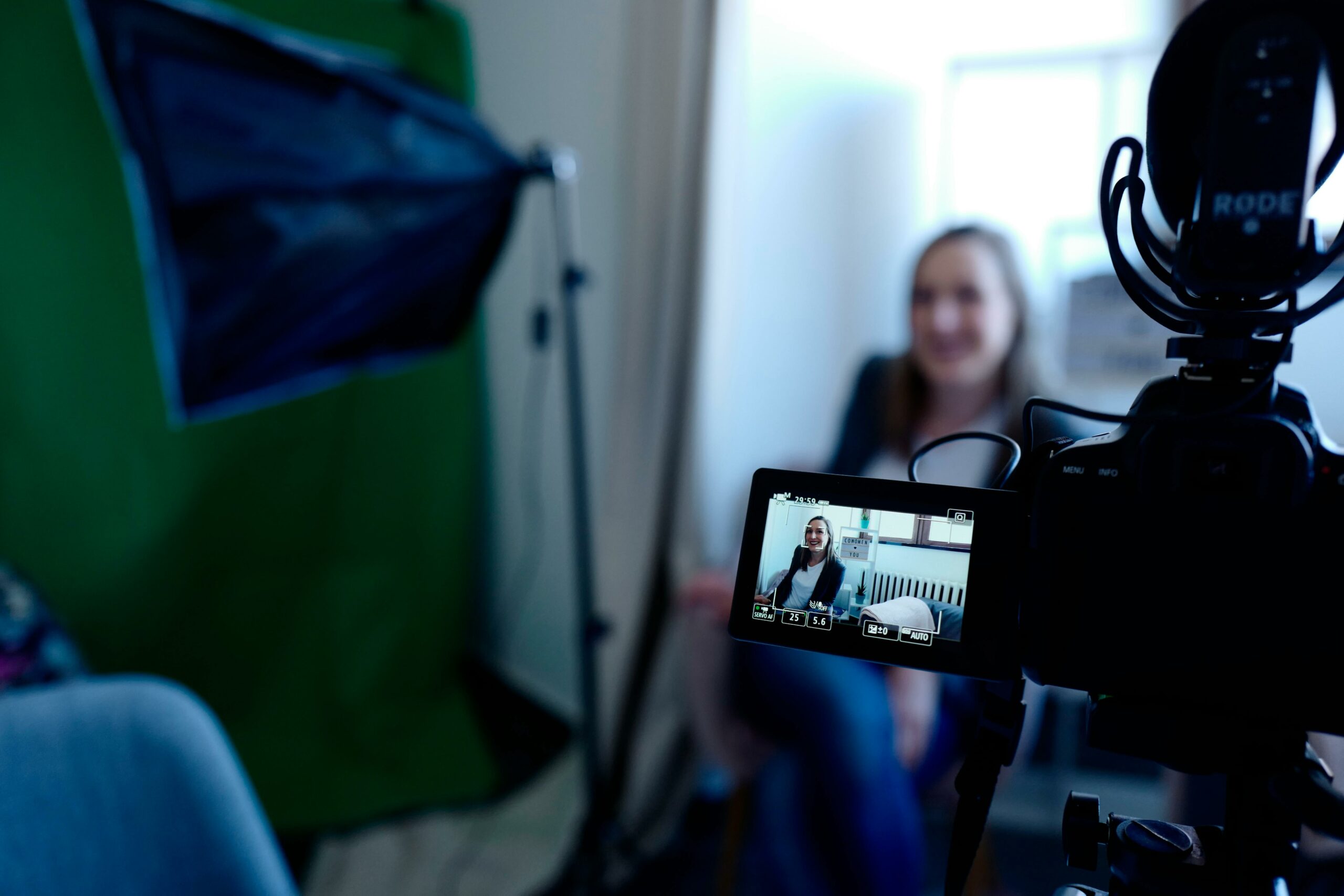 A smiling woman being recorded on camera with a green screen in the background.