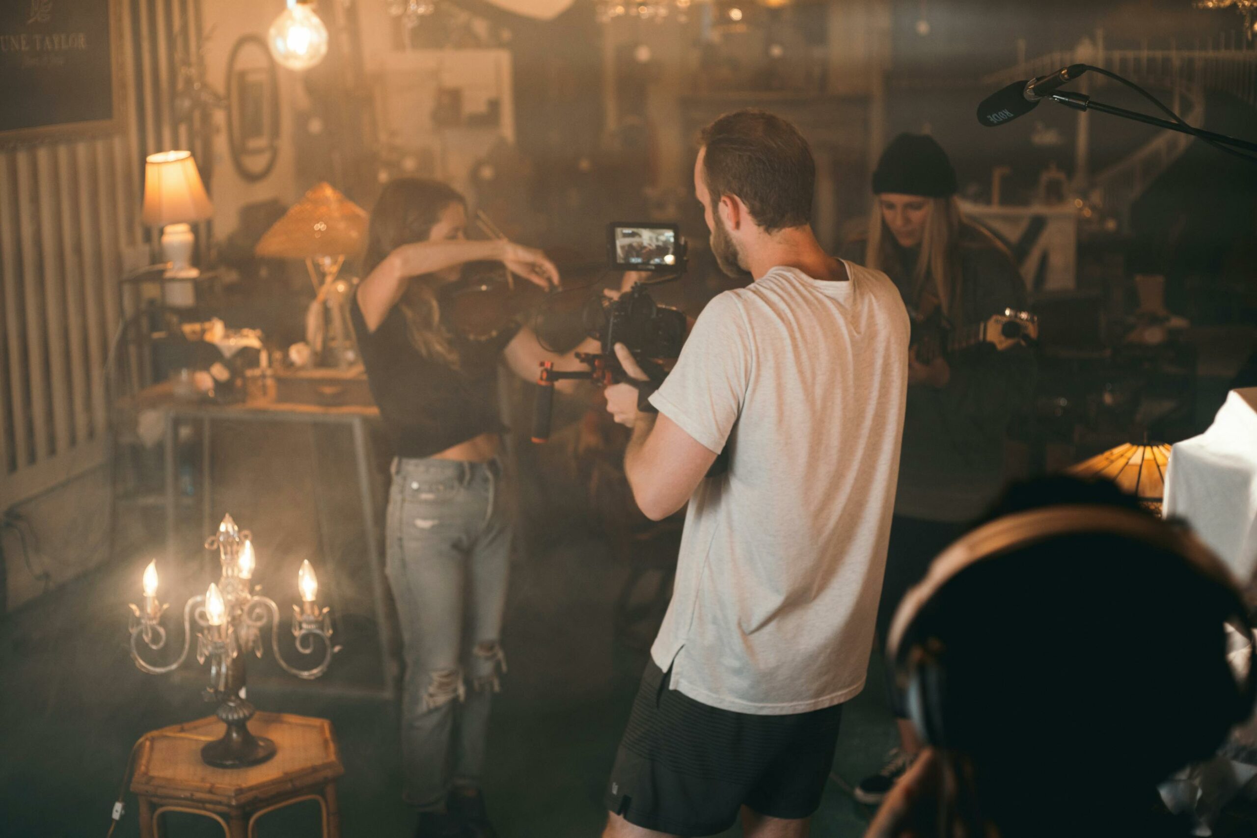 A violinist being filmed in a vintage-inspired setting filled with warm, ambient lighting.