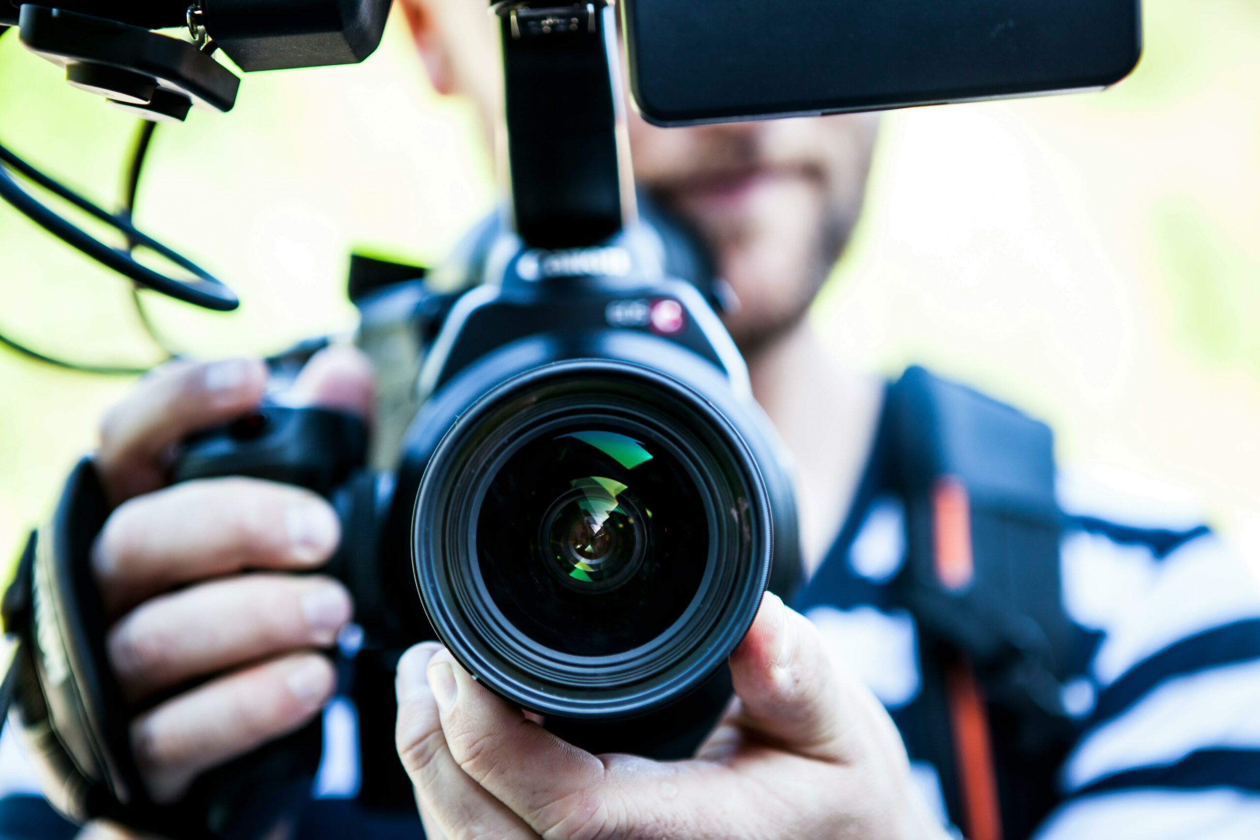 Close-up of a camera lens and microphone held by a videographer, with the focus on the equipment.